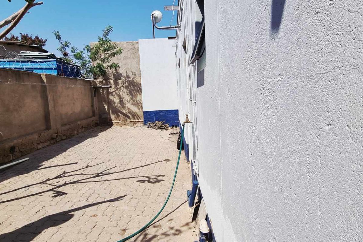 A side courtyard area featuring paved flooring, a perimeter wall, and an external water tap.
