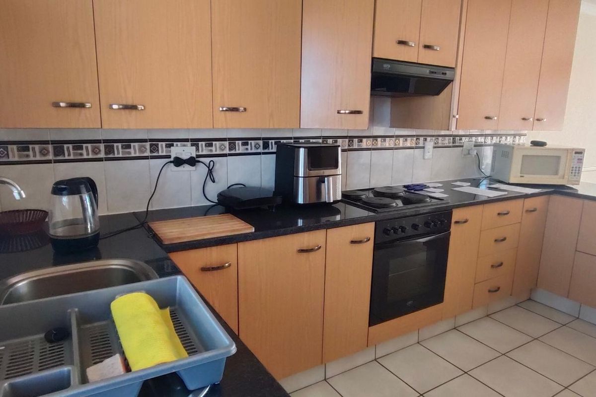 A functional kitchen featuring light wood-finish cabinetry, dark granite countertops, built-in oven, electric hob, and tiled flooring.