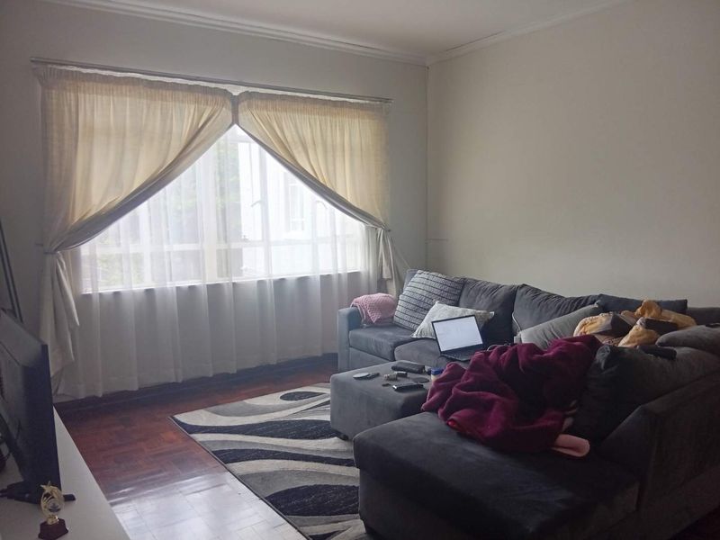 A living room featuring parquet flooring and a large window with natural light, providing a comfortable and functional space.