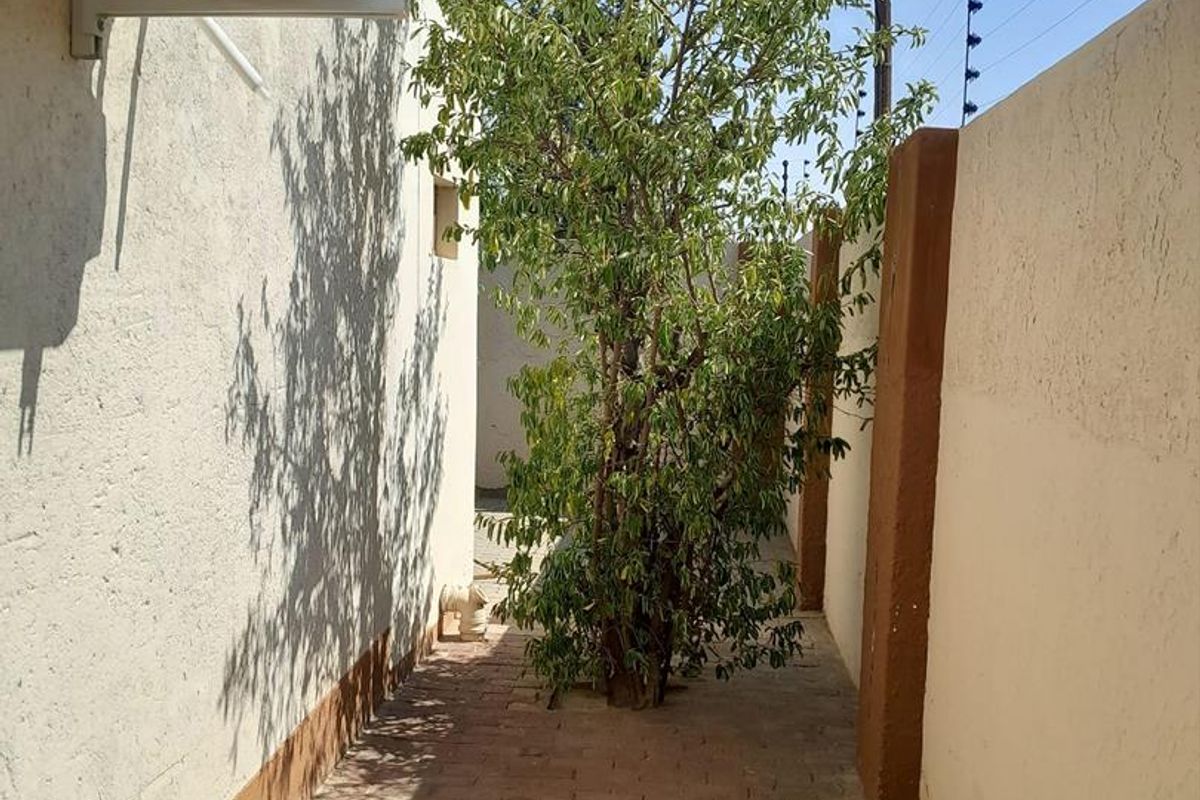 A side exterior walkway featuring brick paving, a mature tree, and a wall-mounted air conditioning unit.