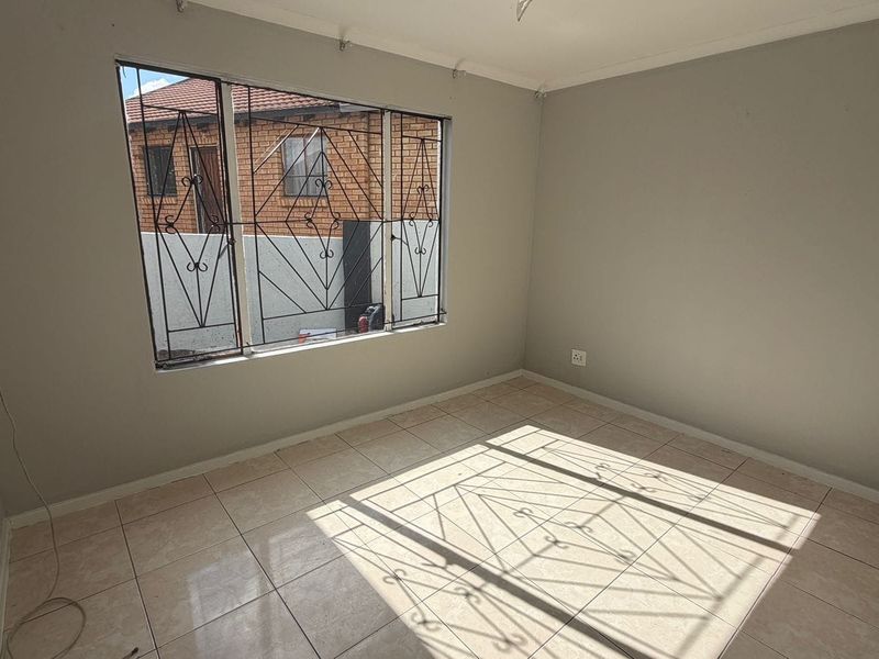 An empty bedroom featuring tiled flooring and security burglar bars on the window, requiring minor cosmetic updates to improve its overall appeal.