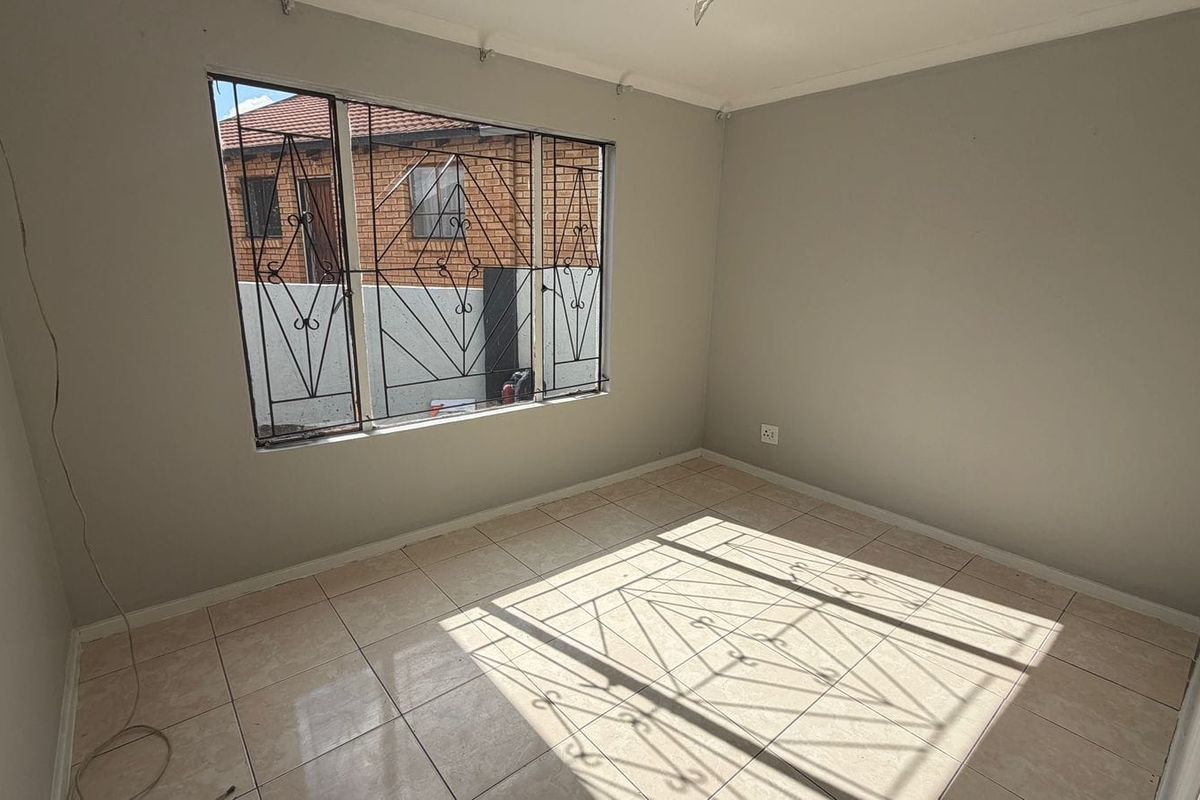 An empty bedroom featuring tiled flooring and security burglar bars on the window, requiring minor cosmetic updates to improve its overall appeal.