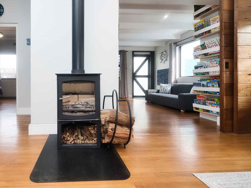 Spacious living area featuring hardwood flooring, a prominent freestanding wood-burning fireplace, and a warm timber-clad feature wall with integrated shelving.