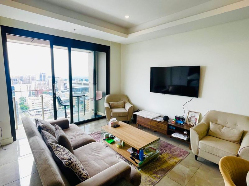 A bright living room featuring tiled floors, a recessed ceiling, and large sliding glass doors opening onto a balcony with city views.