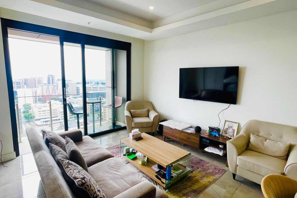 A bright living room featuring tiled floors, a recessed ceiling, and large sliding glass doors opening onto a balcony with city views.