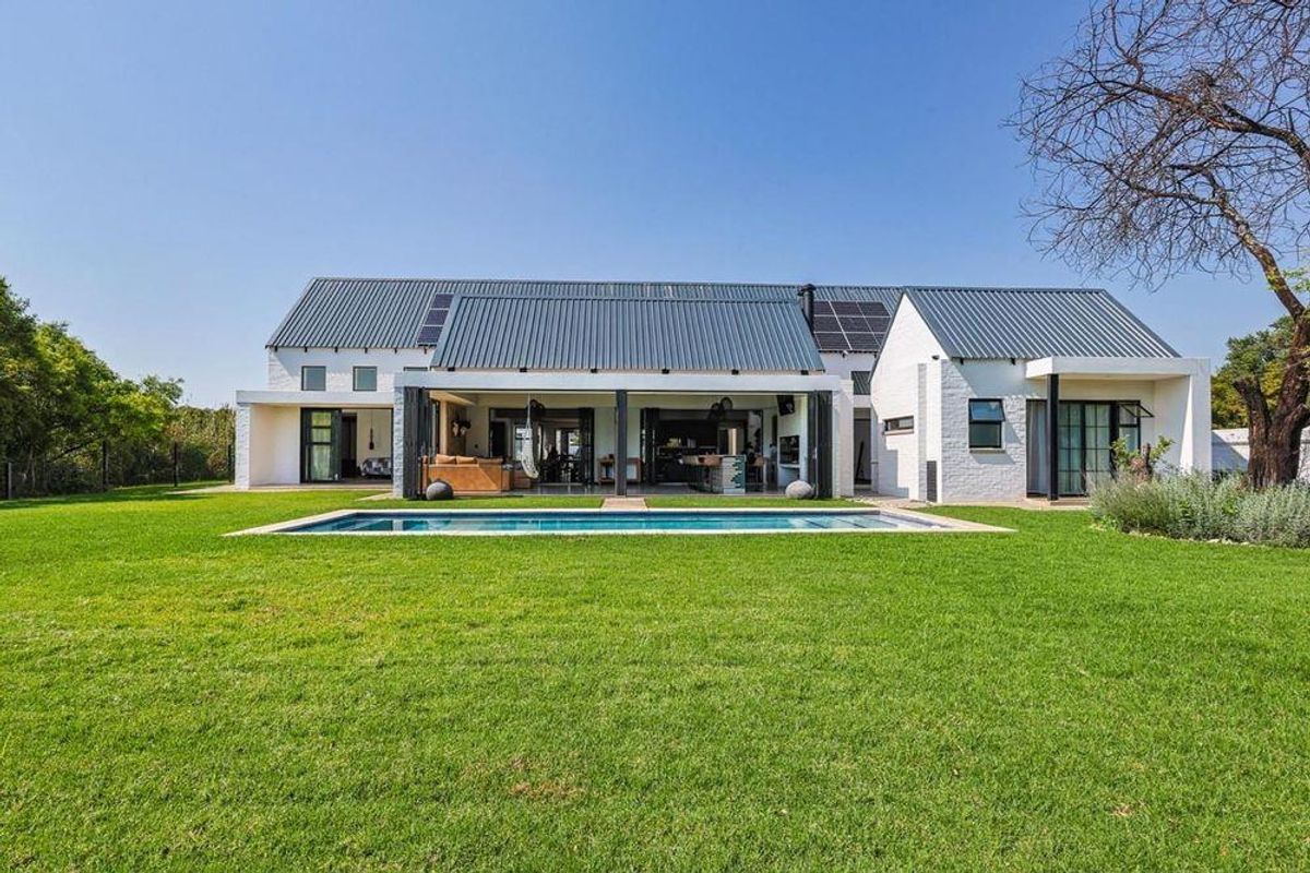 Rear view of a modern farmhouse-style home featuring a swimming pool, expansive lawn, metal roofing with solar panels, and a spacious covered patio area.
