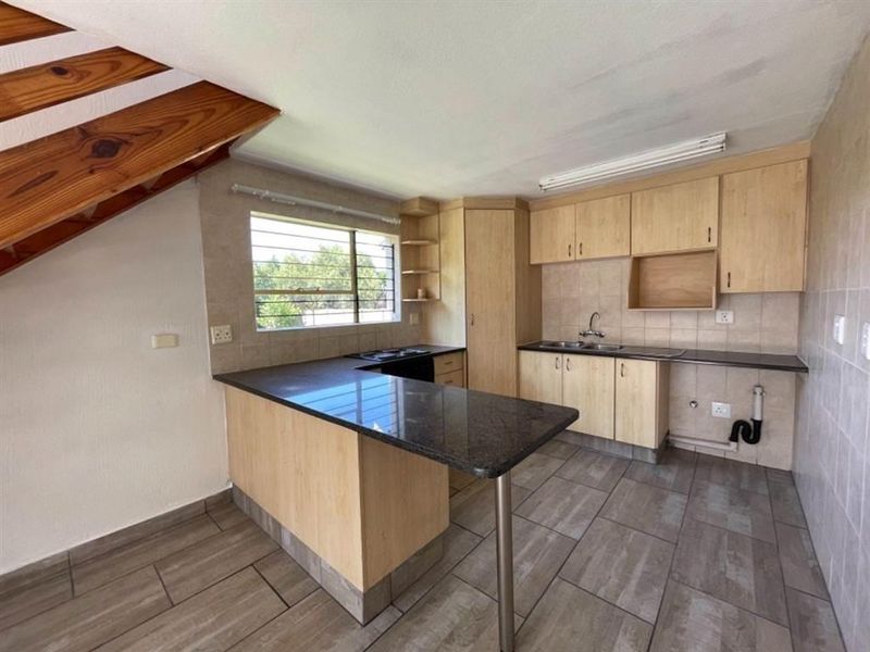 Functional kitchen featuring light wood cabinetry, granite countertops, a double basin sink, and tiled flooring, situated beneath a staircase.