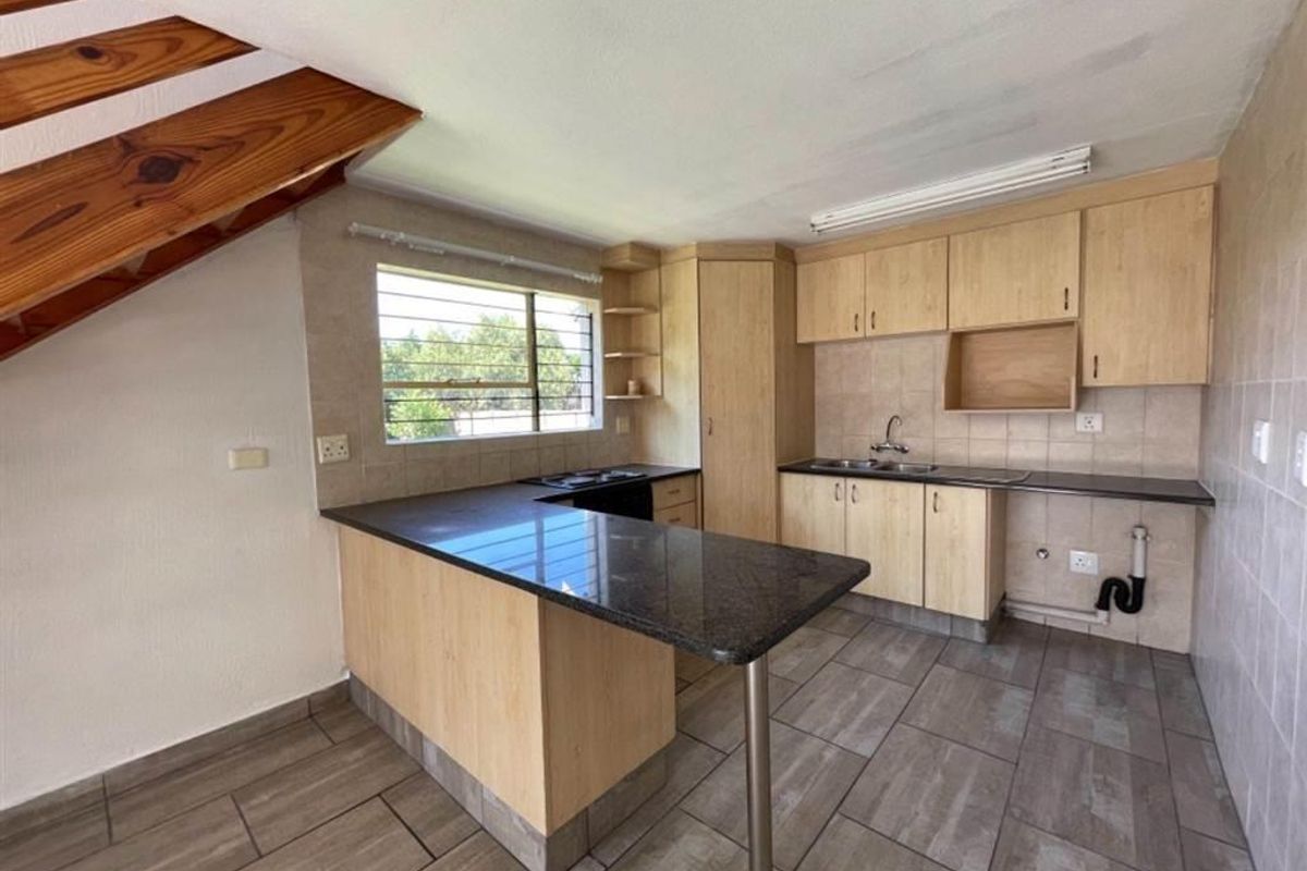 Functional kitchen featuring light wood cabinetry, granite countertops, a double basin sink, and tiled flooring, situated beneath a staircase.