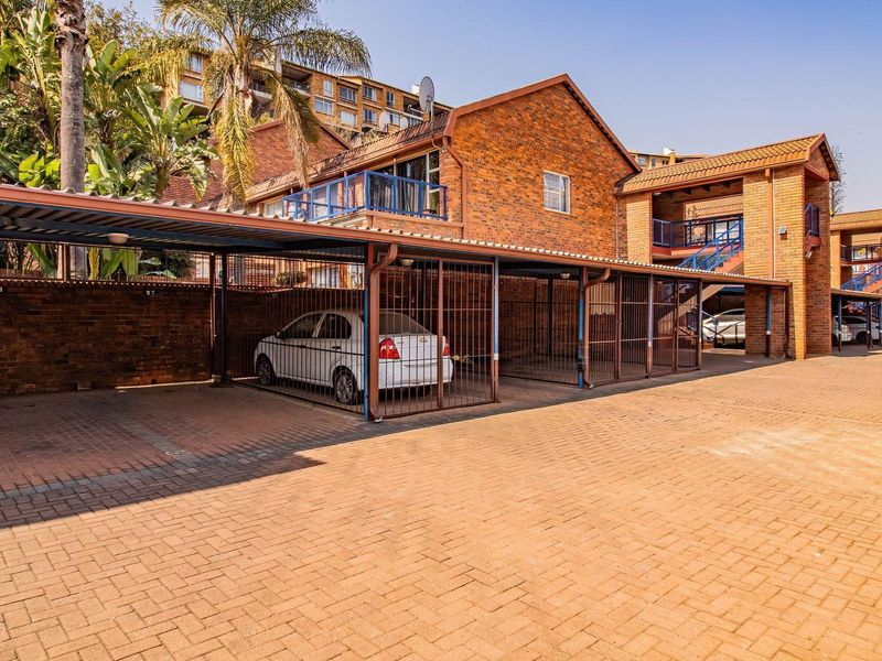 A view of the apartment complex exterior featuring covered parking bays with secure metal gates and paved driveway access.