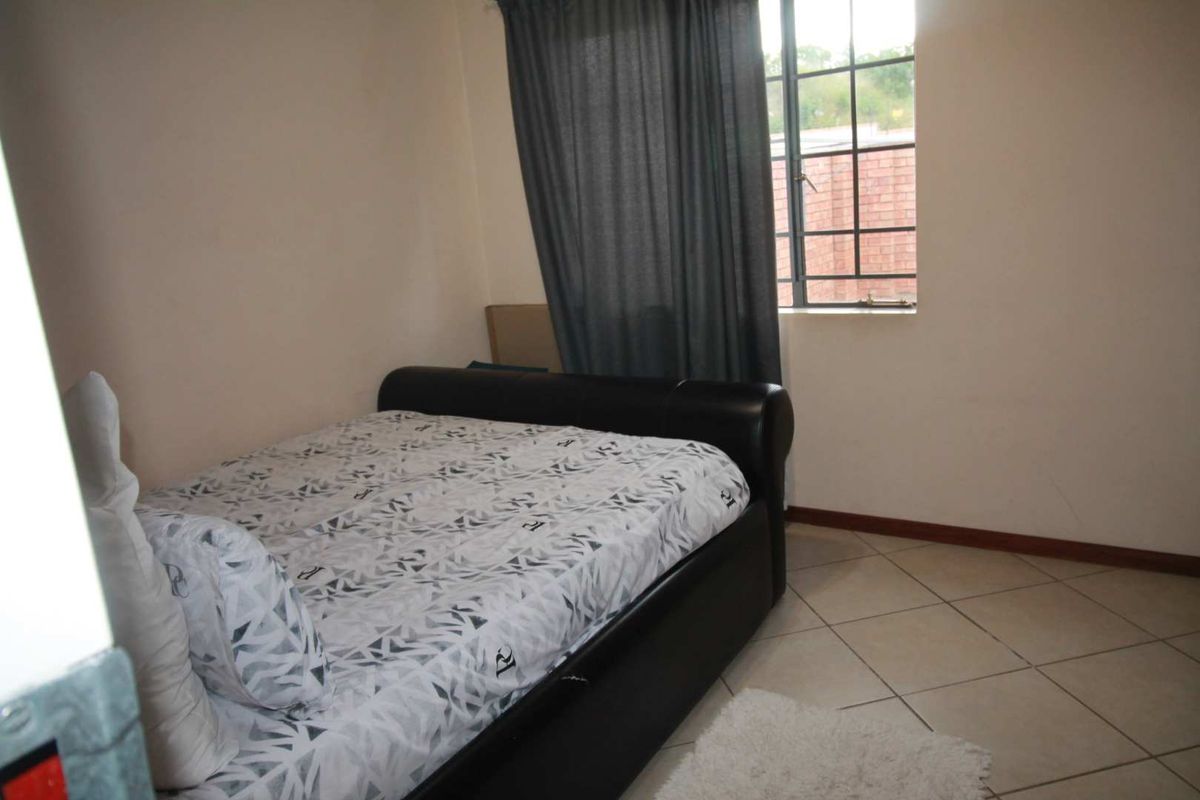 A standard bedroom featuring tiled flooring and a window with security bars, providing natural light and a functional living space.
