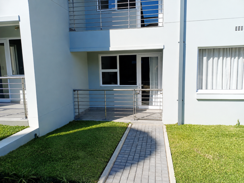 Ground floor apartment exterior featuring a paved walkway leading to a private tiled patio with stainless steel balustrades and modern aluminum window frames.
