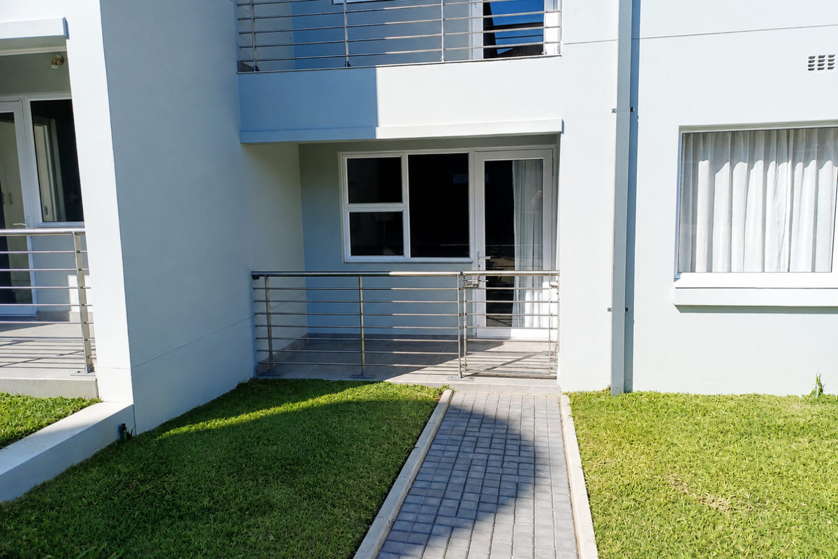 Ground floor apartment exterior featuring a paved walkway leading to a private tiled patio with stainless steel balustrades and modern aluminum window frames.