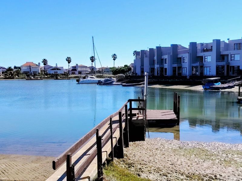 A scenic waterfront view featuring a private jetty and boat slipway, overlooking a tranquil lagoon with surrounding residential properties.
