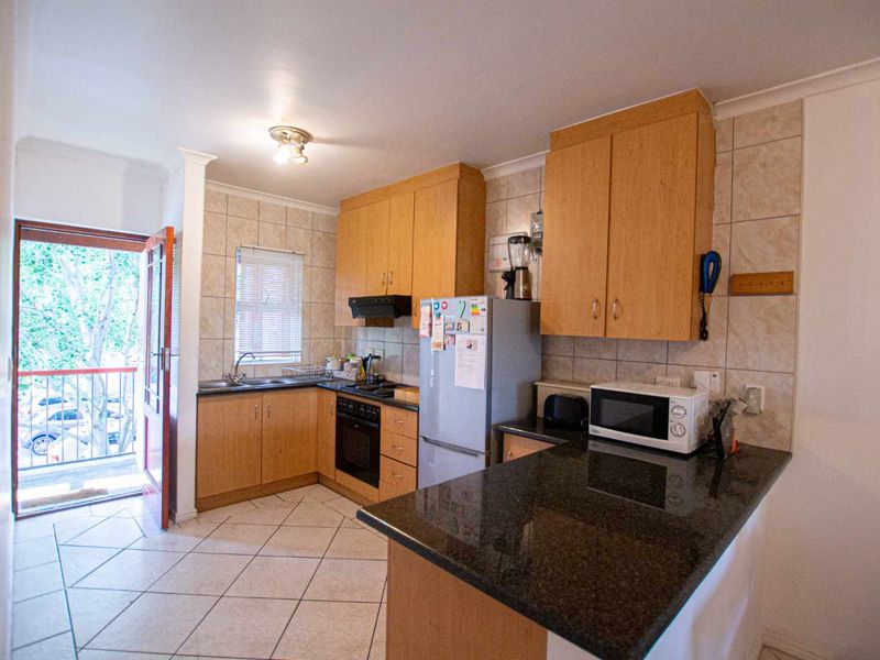 Functional kitchen featuring light wood cabinetry, granite countertops, tiled backsplash, and direct access to a balcony area.