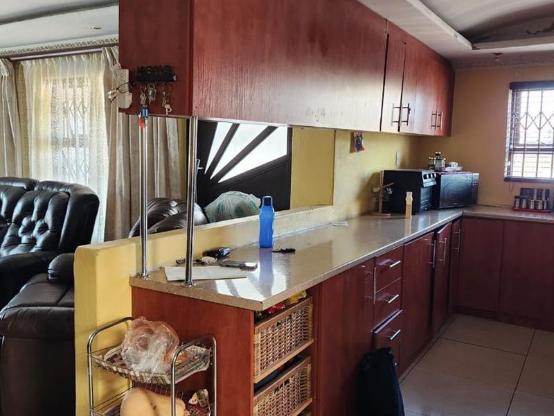 A functional kitchen featuring wood-tone cabinetry, laminate countertops, and tiled flooring, open to the adjacent living area.