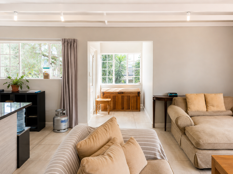 Bright open-plan living area featuring exposed ceiling beams, tiled flooring, and large windows providing natural light and garden views.