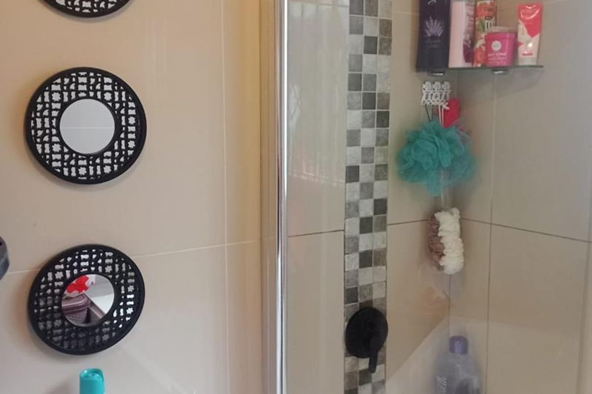A functional bathroom featuring a shower with a glass screen, mosaic tile accents, and neutral wall tiling.