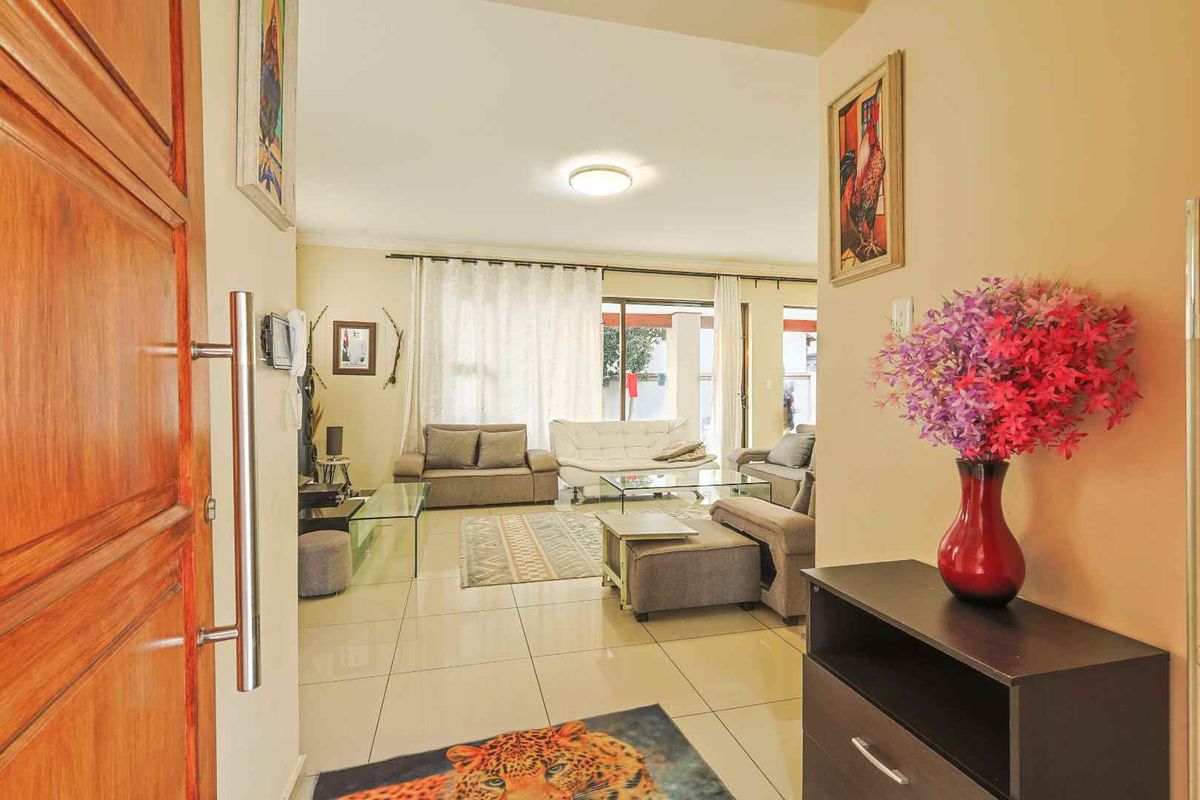 A bright and open living room featuring large format floor tiles, neutral walls, and a sliding glass door providing access to the outdoor area.