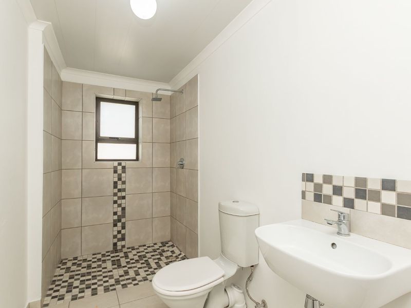 A clean, functional bathroom featuring a walk-in shower, white toilet, and wall-mounted washbasin with decorative tiled accents.