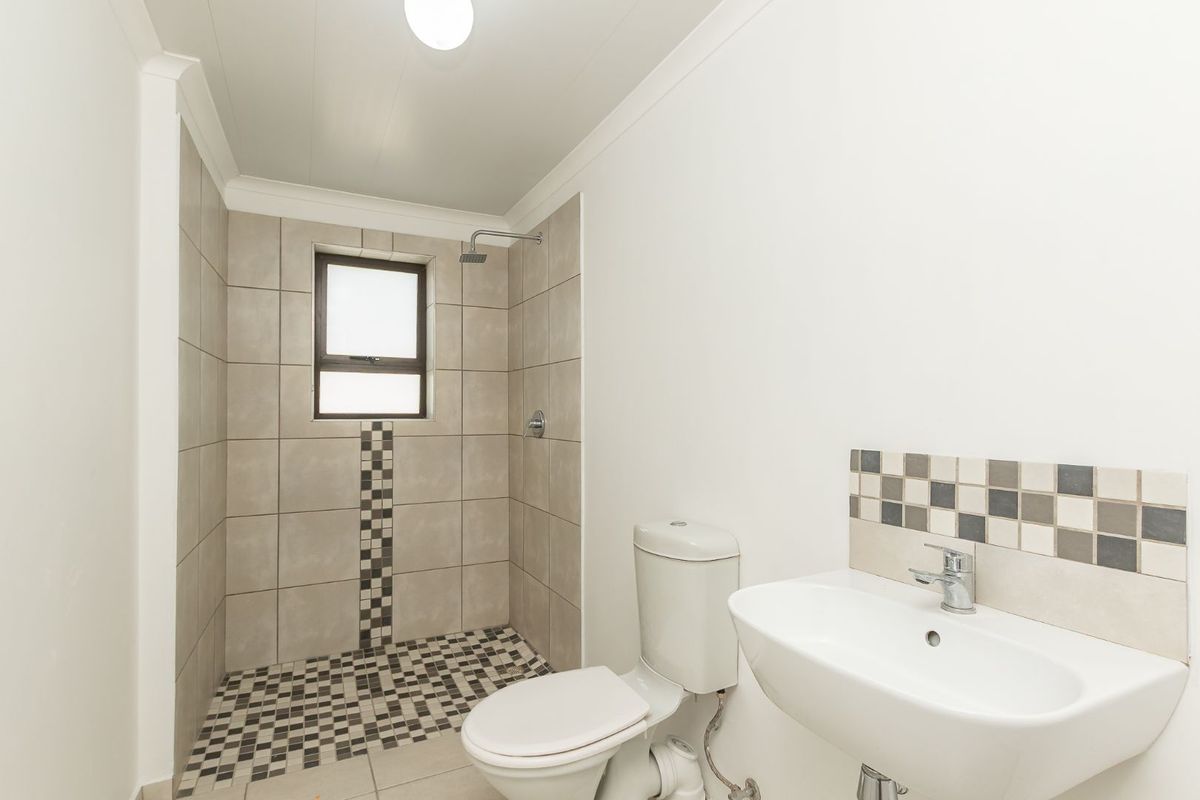 A clean, functional bathroom featuring a walk-in shower, white toilet, and wall-mounted washbasin with decorative tiled accents.