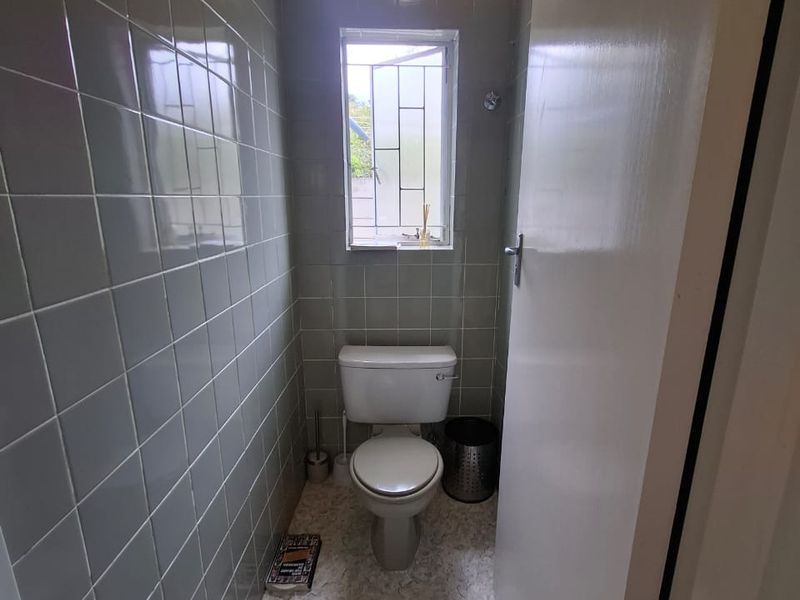 A compact guest bathroom featuring full-height wall tiling, vinyl flooring, and a window with security bars.