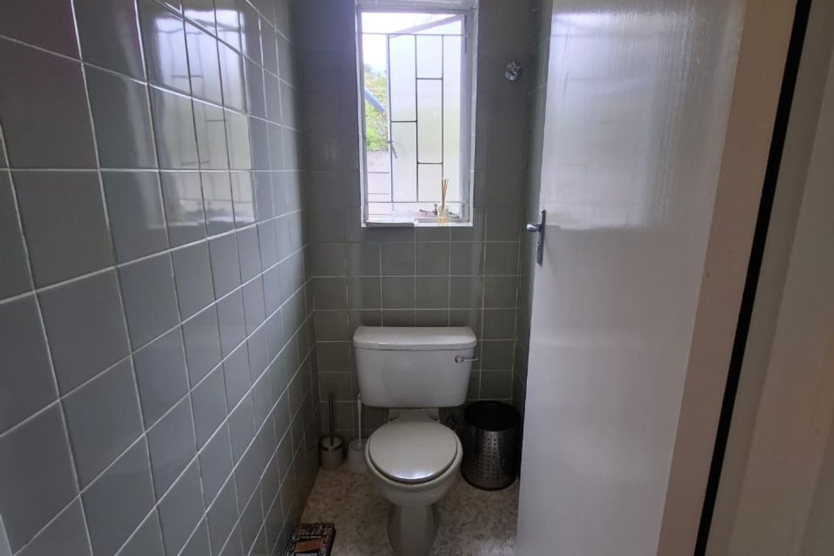 A compact guest bathroom featuring full-height wall tiling, vinyl flooring, and a window with security bars.
