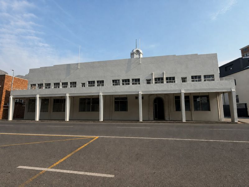 A prominent Art Deco style commercial building featuring a distinctive clock tower, a covered colonnade, and a clean white facade.
