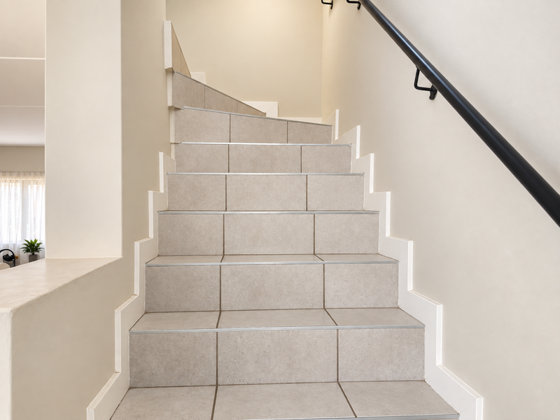 A clean, well-maintained staircase featuring neutral-toned floor tiles and a modern black metal handrail, providing a bright and functional transition between levels.