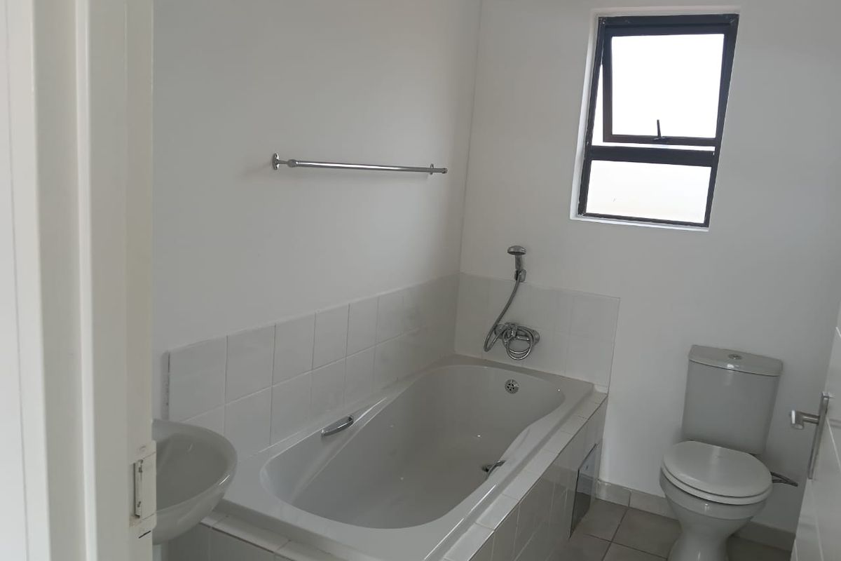 A functional bathroom featuring a built-in bathtub with shower mixer, a standard toilet, and tiled flooring.