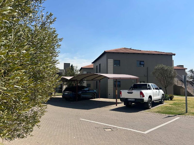 Front exterior view of the townhouse complex featuring a paved driveway and a covered carport structure.