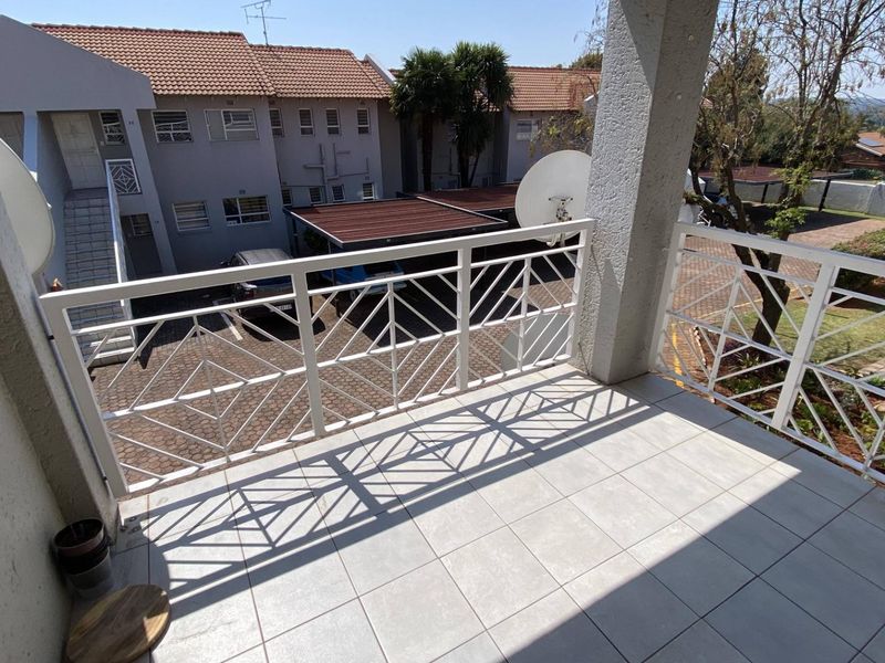 A clean, tiled balcony featuring a white metal balustrade, overlooking the apartment complex parking area and grounds.