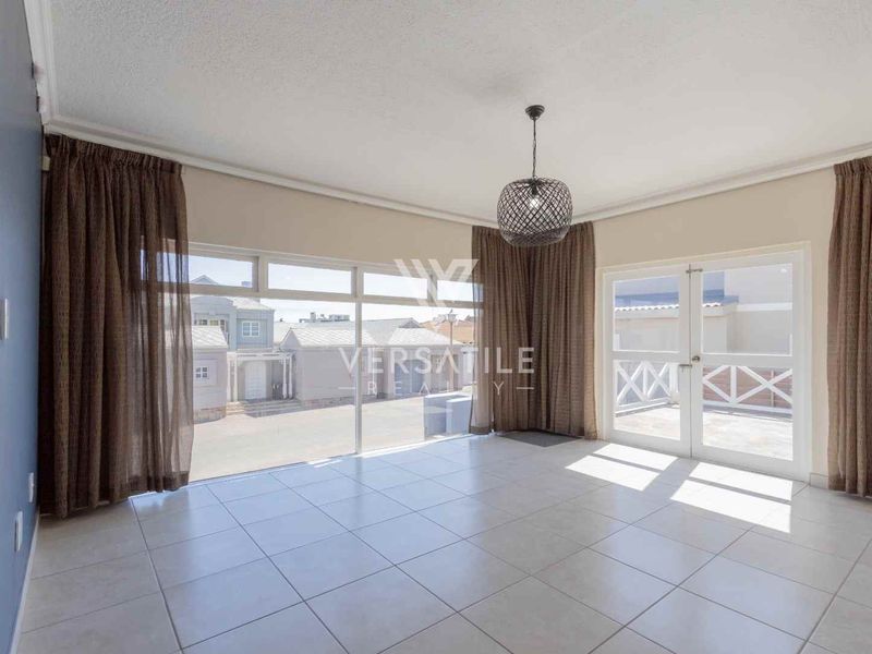 Spacious living area featuring neutral tiled flooring, large glass sliding doors, and double doors leading to an outdoor space, offering ample natural light.