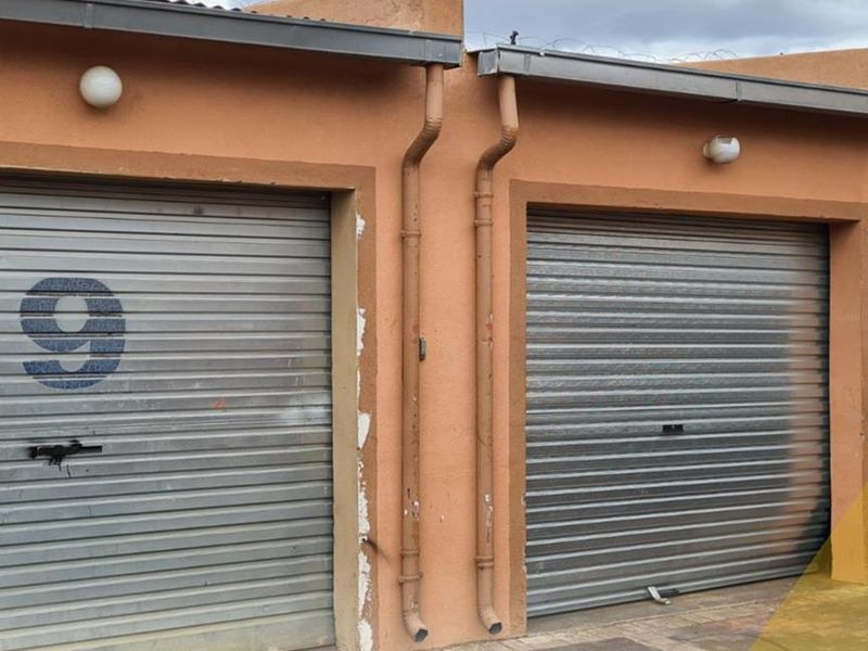 Exterior view of two secure garage units featuring metal roller shutter doors and external wall-mounted lighting.
