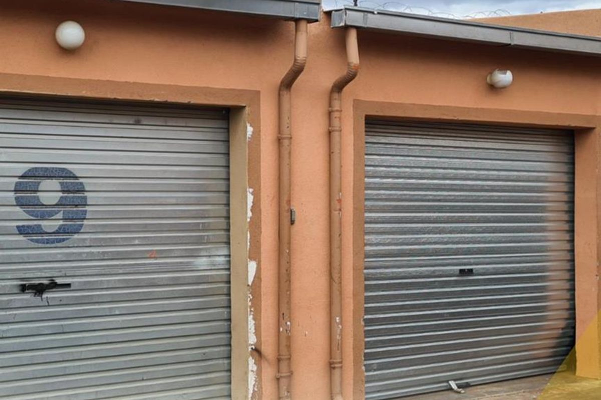 Exterior view of two secure garage units featuring metal roller shutter doors and external wall-mounted lighting.