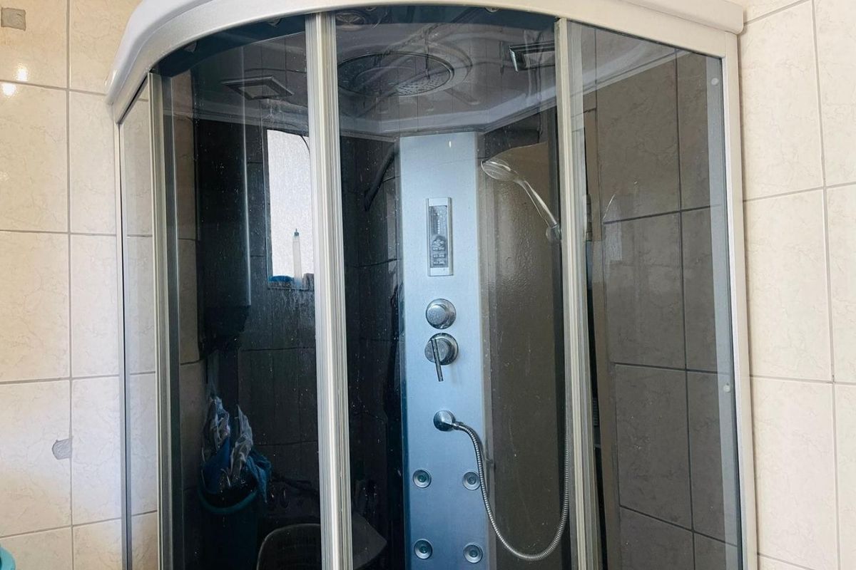 A bathroom featuring a corner shower enclosure with a built-in shower panel and tiled walls.
