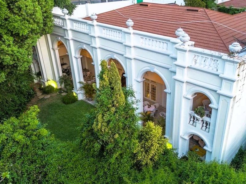 Aerial view of the rear facade featuring a classic arched colonnade, decorative balustrade, terracotta roof, and a lush, well-maintained garden area.