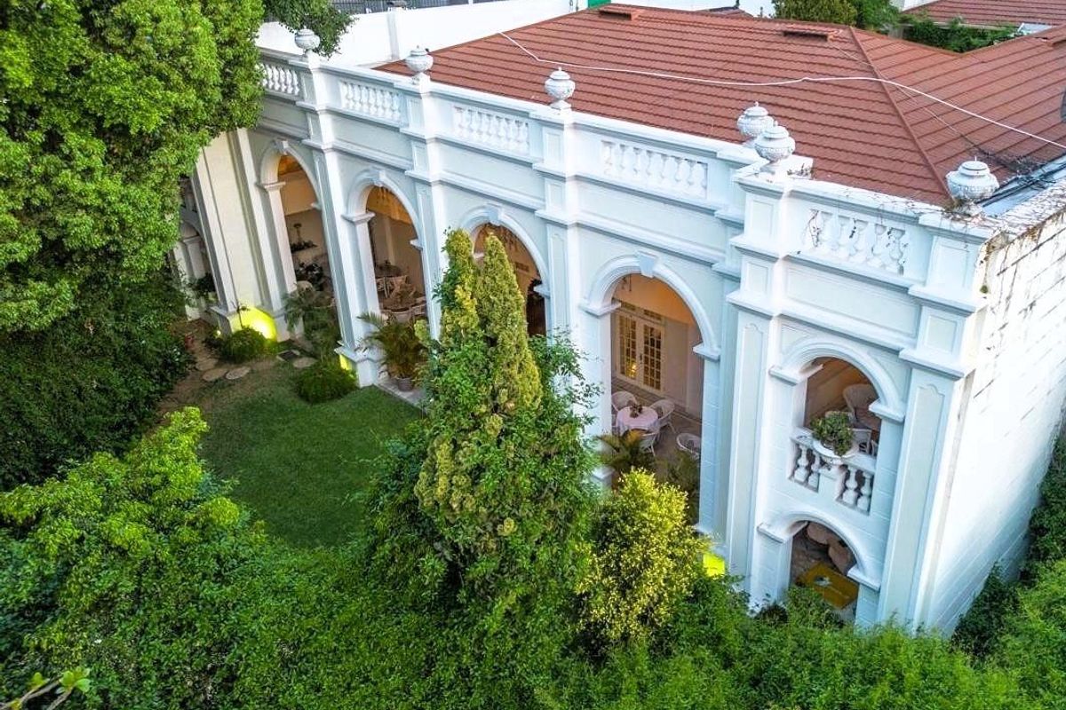 Aerial view of the rear facade featuring a classic arched colonnade, decorative balustrade, terracotta roof, and a lush, well-maintained garden area.