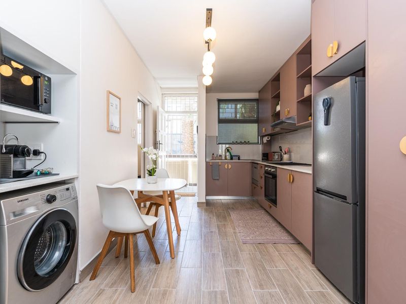 Modern galley-style kitchen featuring sleek mauve cabinetry, integrated appliances, wood-look tiled flooring, and a dedicated laundry nook with built-in shelving.