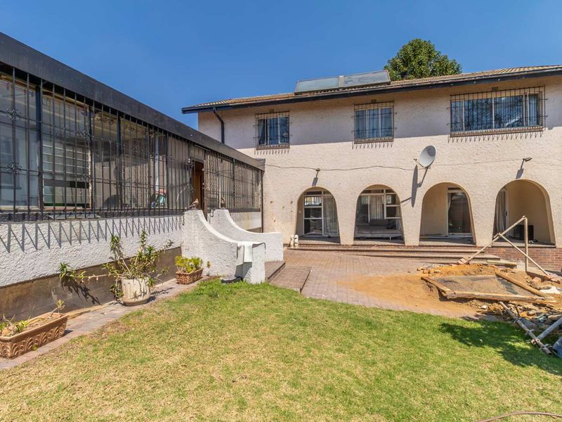 Rear view of the property featuring an arched patio area, paved courtyard, and security bars on windows, with ongoing exterior maintenance visible.