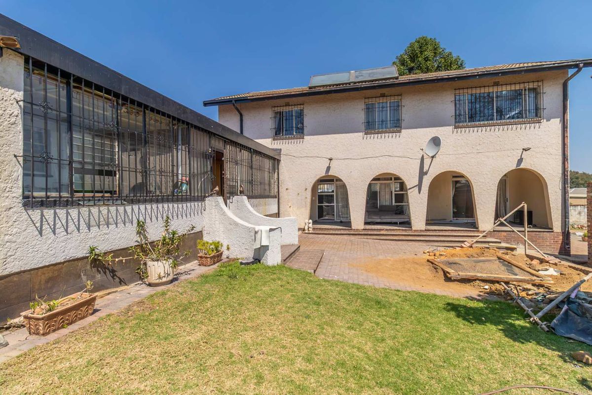Rear view of the property featuring an arched patio area, paved courtyard, and security bars on windows, with ongoing exterior maintenance visible.