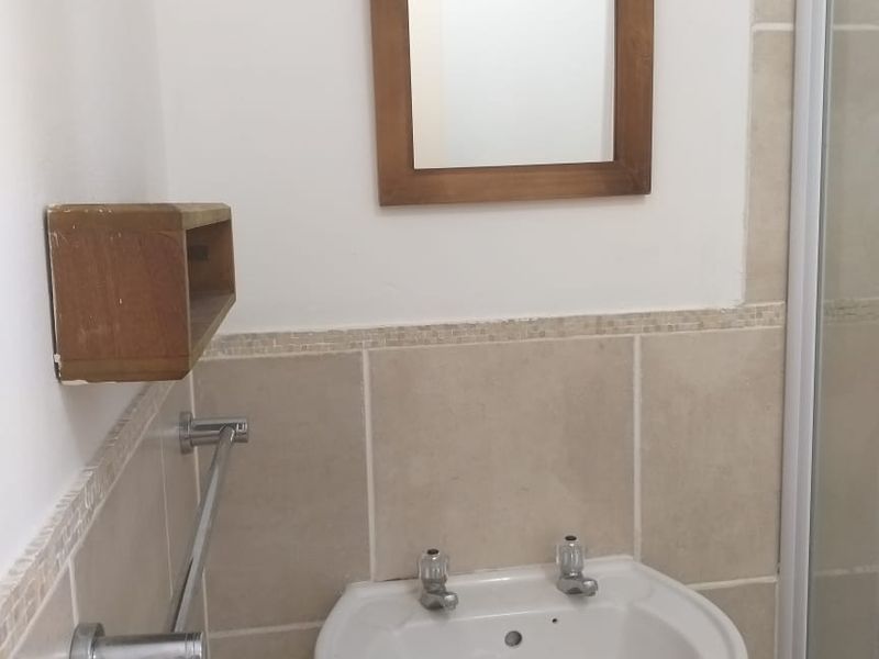 A functional bathroom featuring a pedestal basin with chrome taps, tiled splashback, and a shower enclosure with a neutral finish.