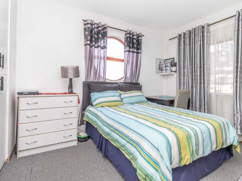 A functional bedroom featuring carpeted flooring, a built-in wardrobe, and a unique arched window, providing a comfortable and practical living space.