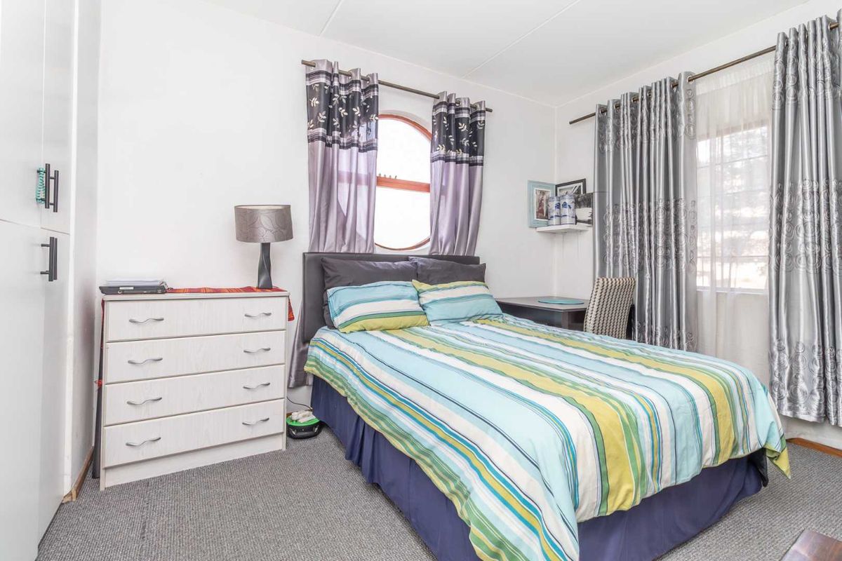 A functional bedroom featuring carpeted flooring, a built-in wardrobe, and a unique arched window, providing a comfortable and practical living space.