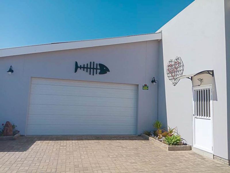 Front elevation featuring a clean sectional garage door, paved driveway, and a secure side entrance with integrated garden bed.