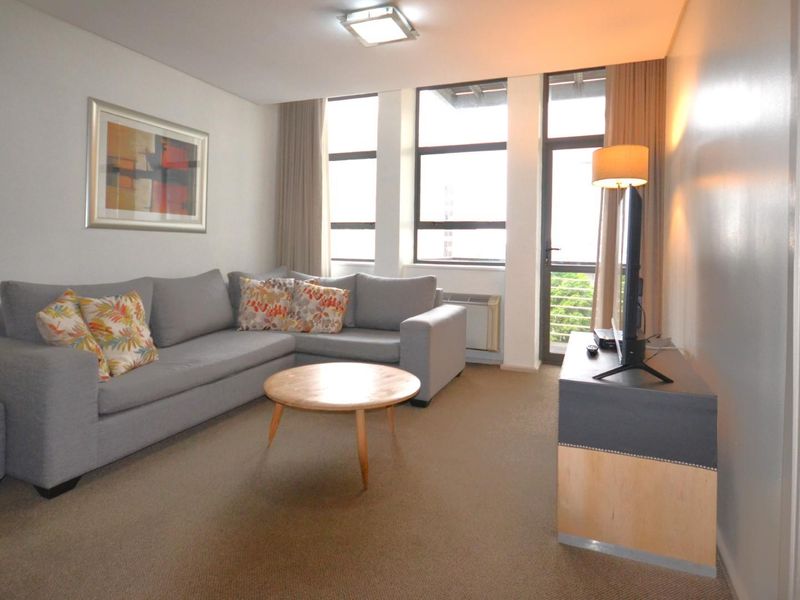 A comfortable living room featuring large windows, carpeted flooring, and direct access to a balcony, providing ample natural light.