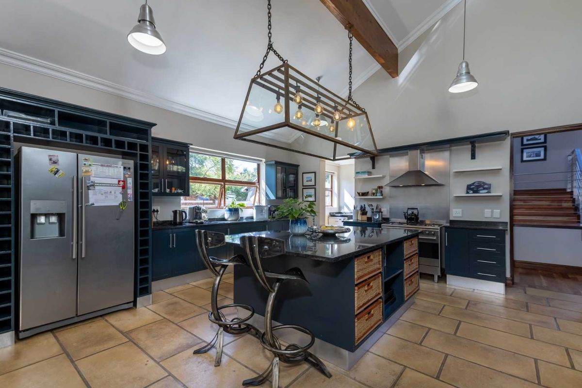 Spacious kitchen featuring dark cabinetry, a large central island with stone countertop, stainless steel appliances, vaulted ceilings with exposed beams, and tiled flooring.