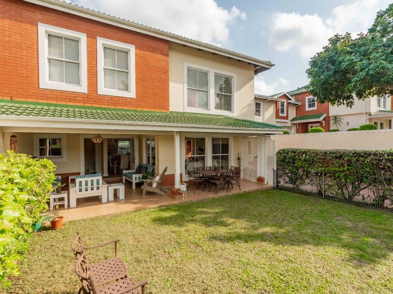 Rear view of the townhouse featuring a covered tiled patio, brick and plaster facade, sash windows, and a private garden area.