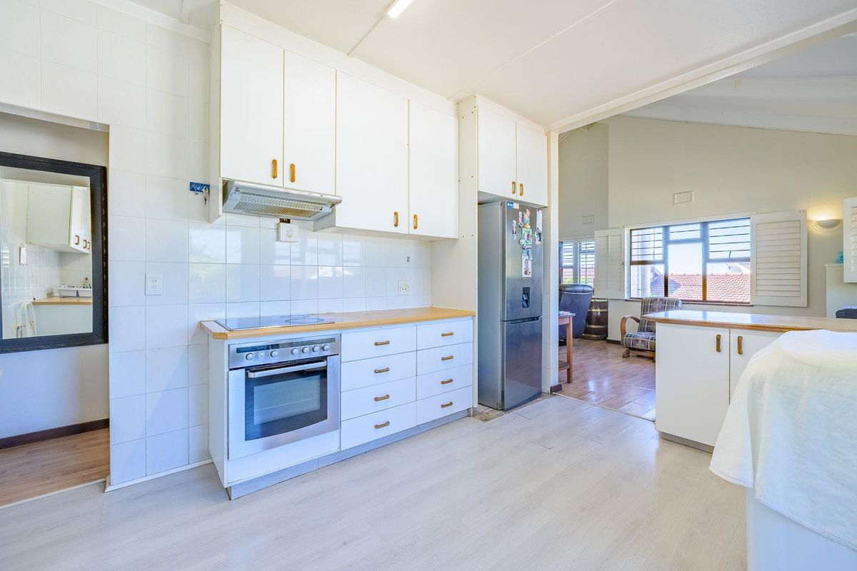 A functional kitchen featuring white cabinetry, a built-in oven and hob, tiled splashbacks, and light-toned laminate flooring, flowing into an adjacent living area.
