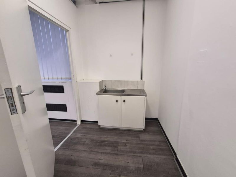 A small utility space featuring a basic stainless steel sink unit, laminate flooring, and exposed ceiling infrastructure.