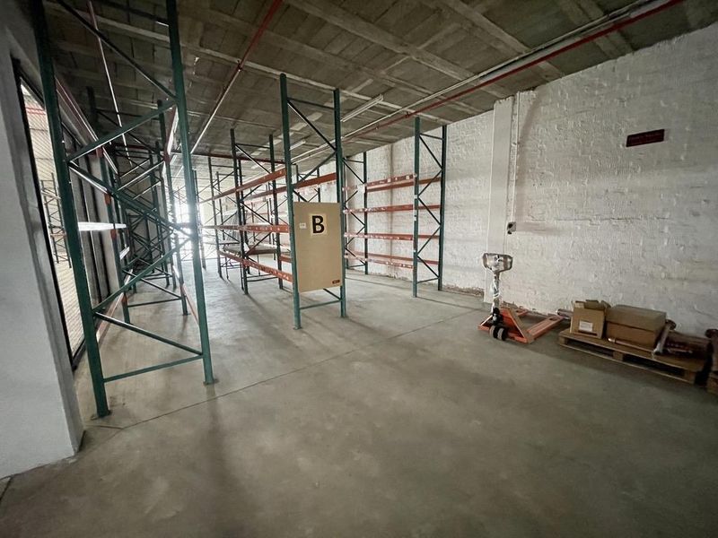 Spacious industrial utility area featuring exposed concrete ceilings, painted brick walls, and fixed metal racking systems suitable for storage or warehouse operations.